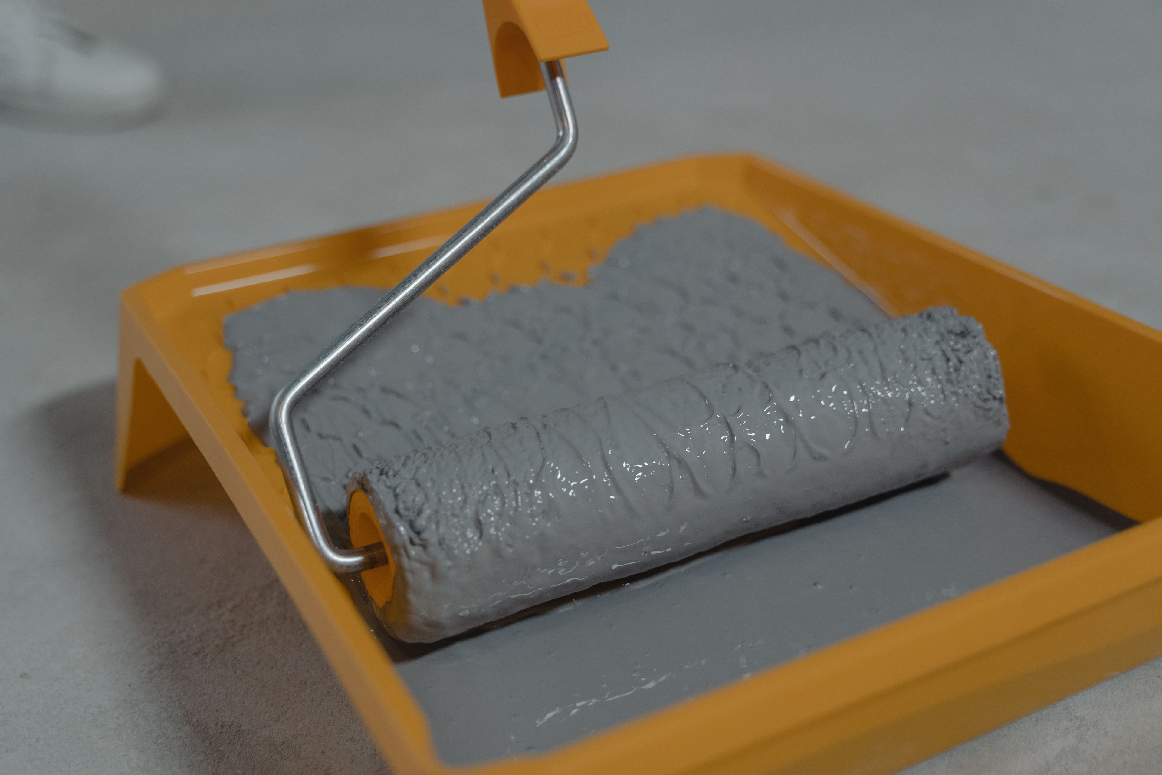 Paint roller resting in a tray of gray paint